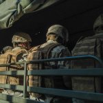 A group of soldiers dressed in full gear sitting in a vehicle.